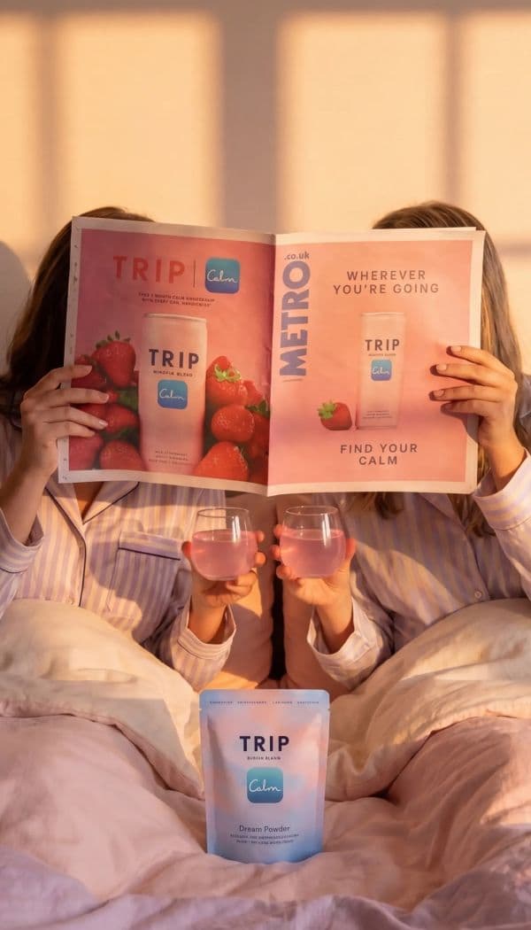 Two women in striped pyjamas read a magazine in bed, holding pink relaxation drinks