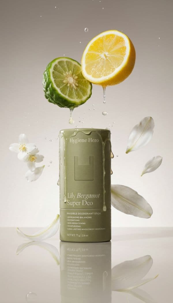 Sage deodorant stick with citrus halves, dripping cream and white petals on a neutral backdrop